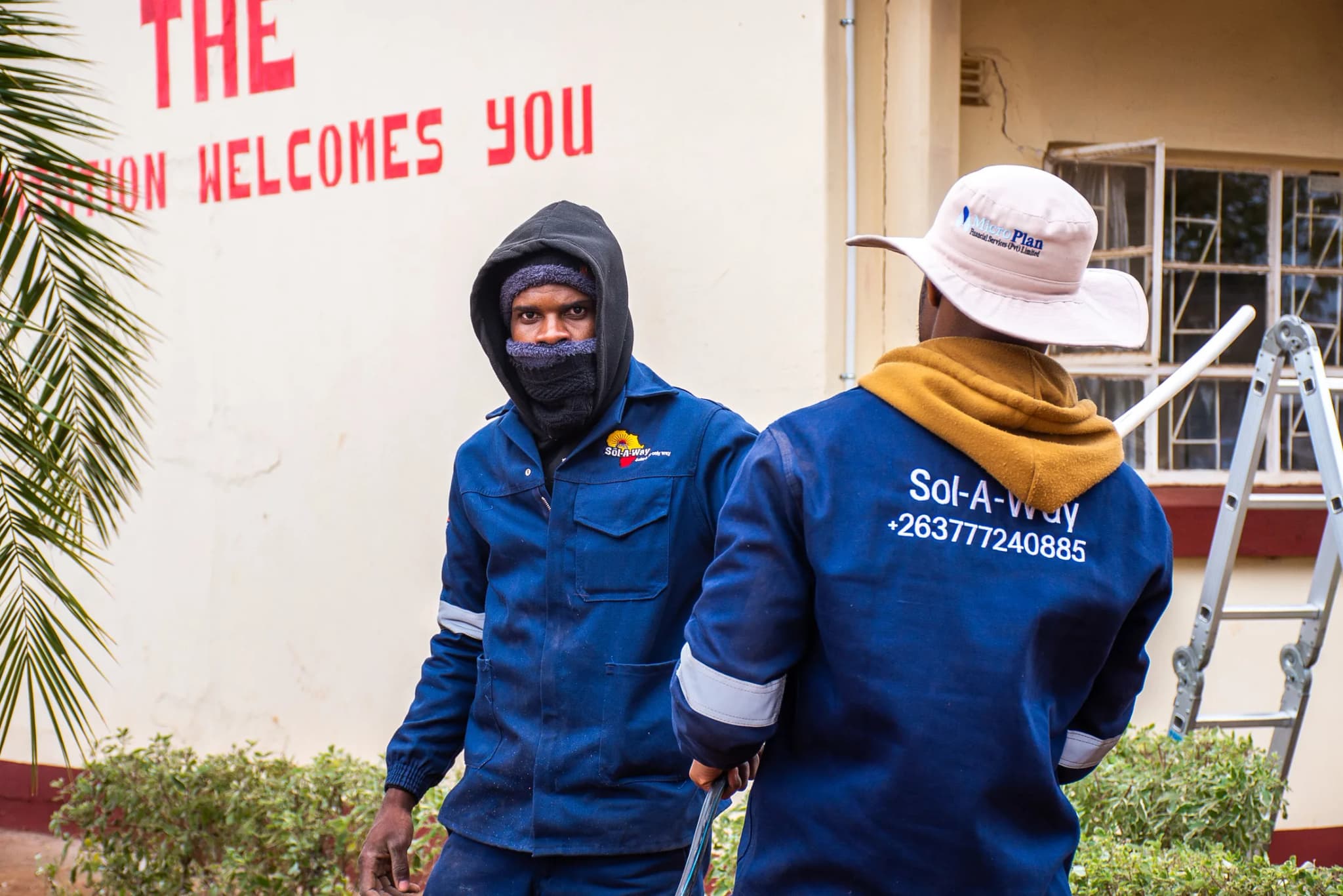 Two Sol-A-Way technicians in branded workwear outside a school building