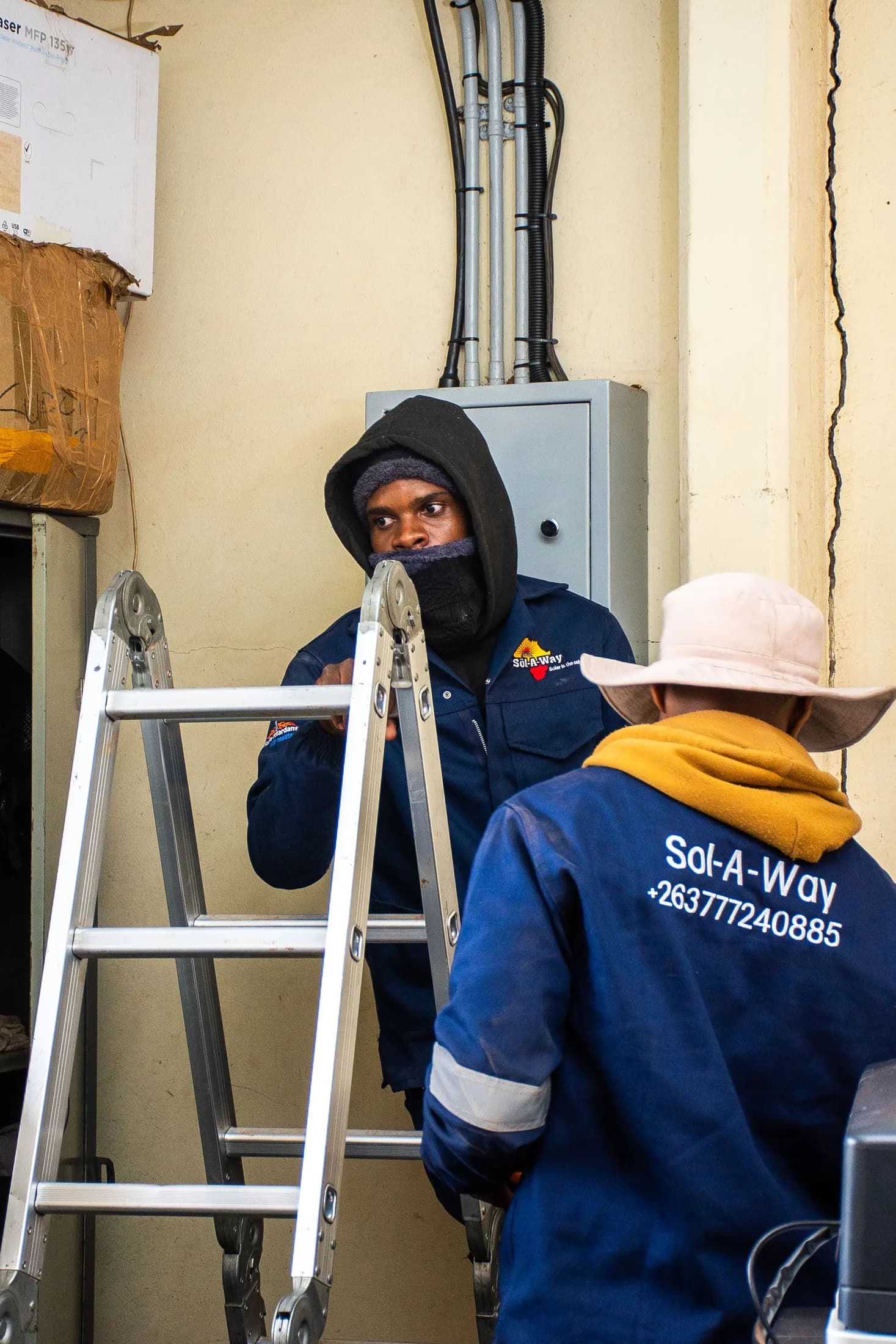 Technicians on a ladder at an indoor distribution board