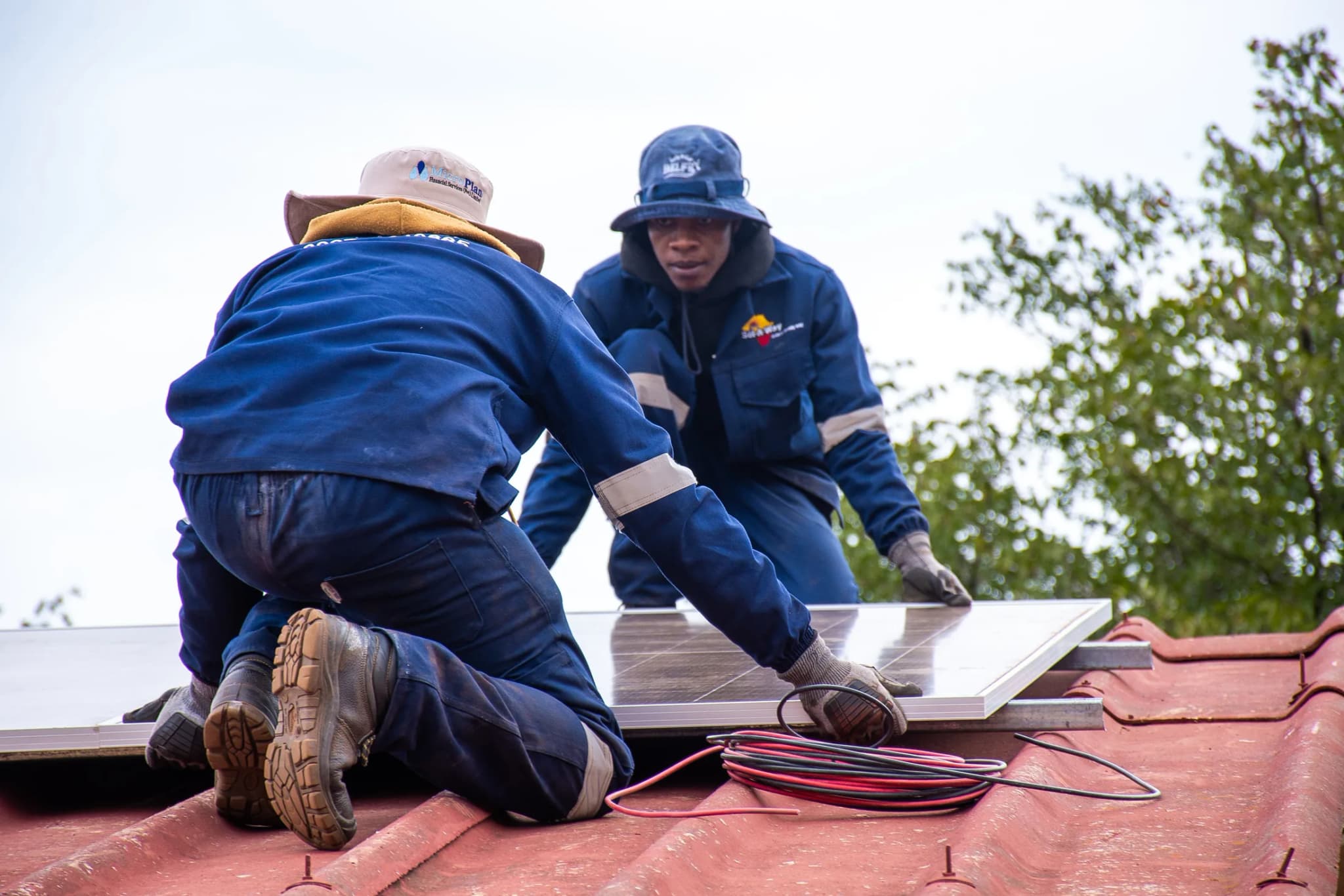 Two technicians laying solar panels on a red school roof