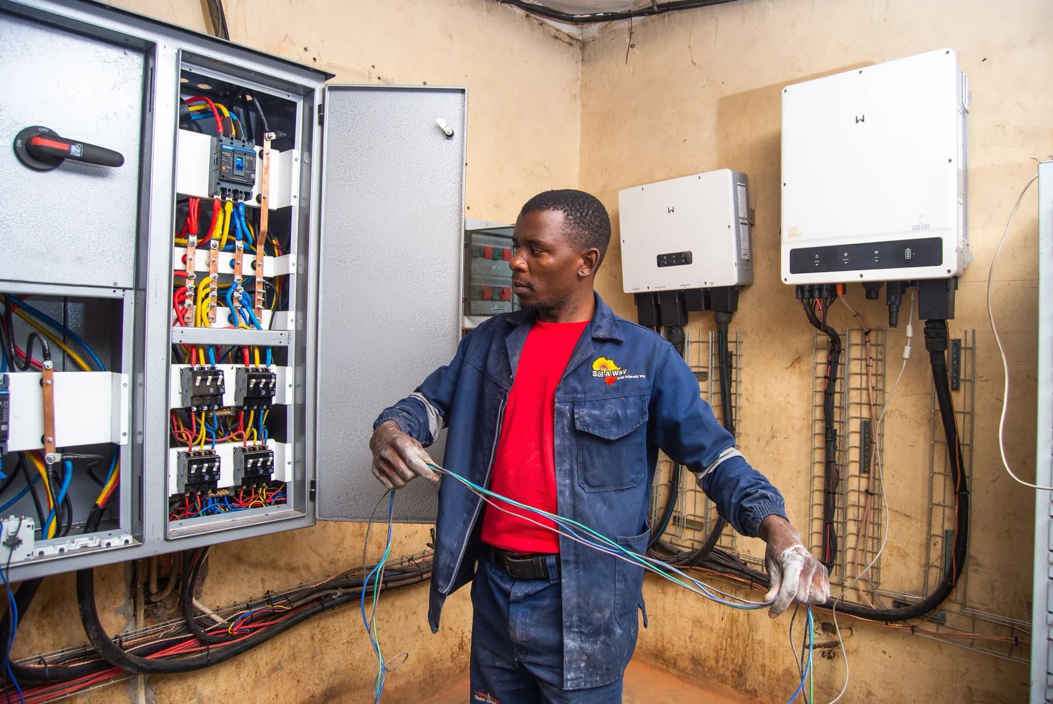 Technician wiring a commercial distribution board beside two inverters