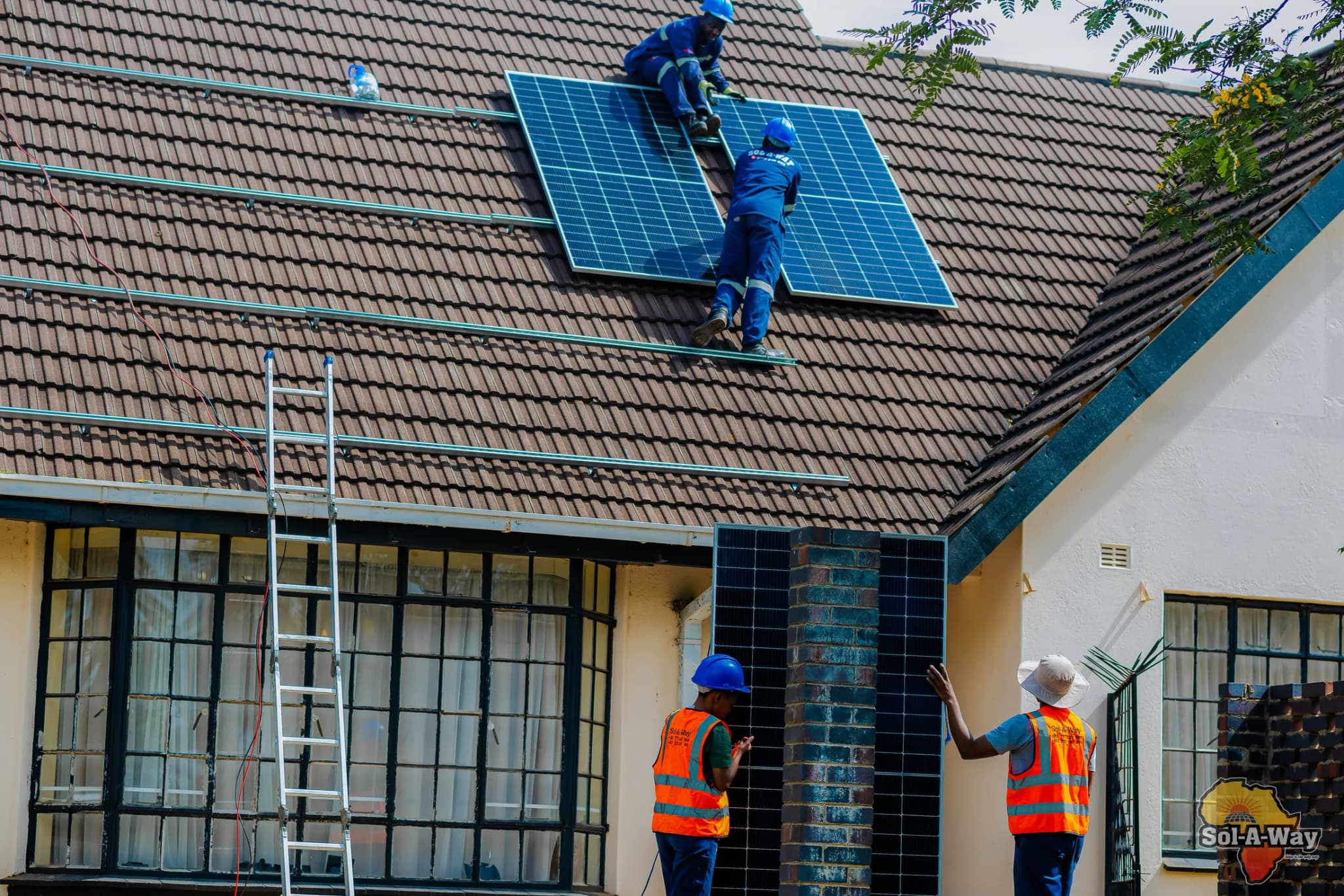 Two technicians on a tiled roof with the first panels in place